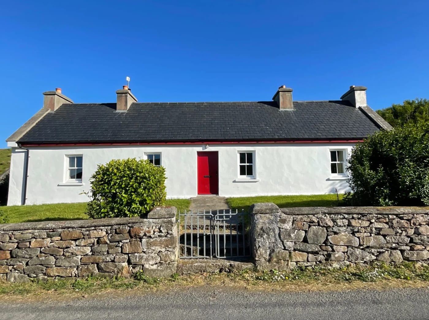 Front view of Clare Island Farmhouse with a red door, whitewashed walls, a low stone wall, and blue sky