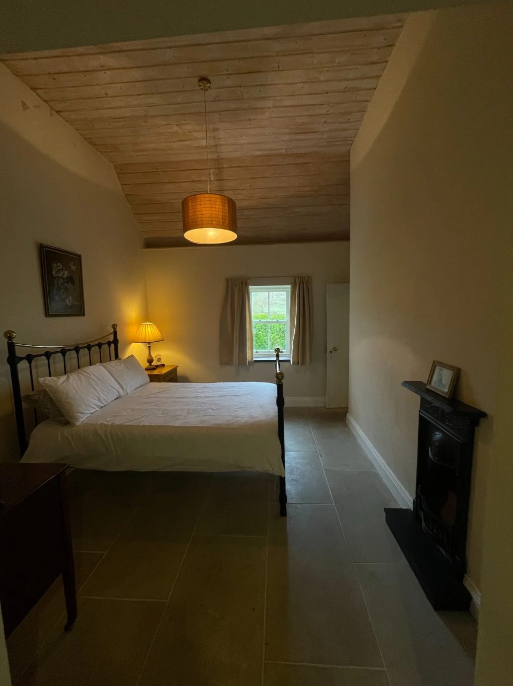 Room 1 double guest room with a black metal bed, warm bedside lamp, timber ceiling, and tiled floor