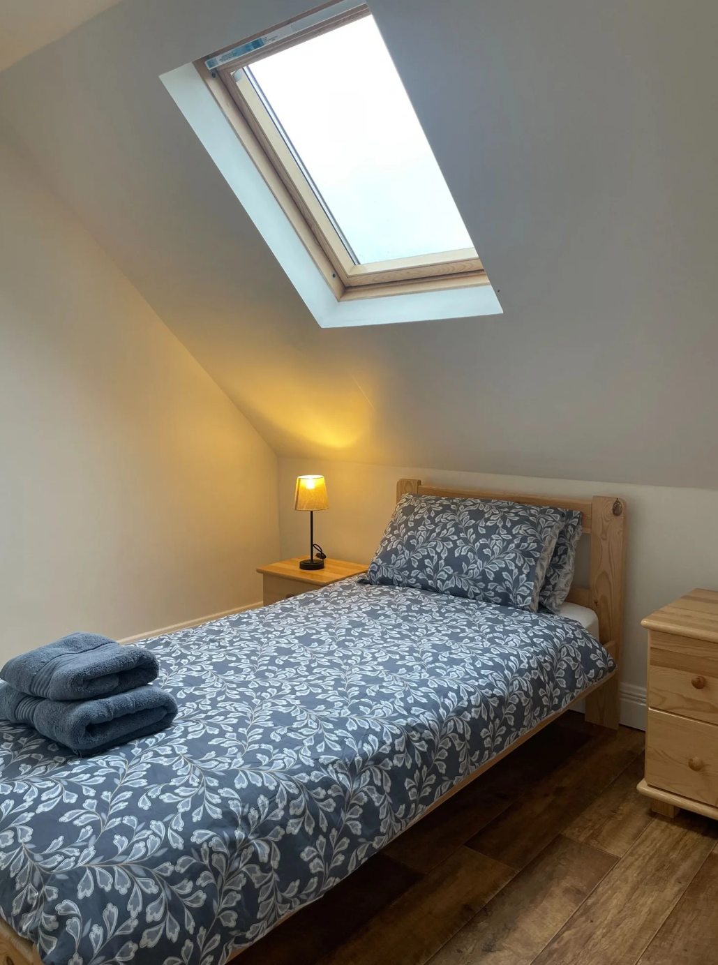 Room 4 twin loft room with a bed, folded towels, sloped ceiling, roof window, and timber floor